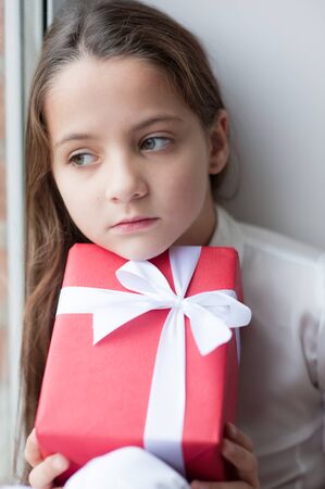 close up of beautiful little girl dreaming by the window holding a box with gift in Christmas Eveの写真素材