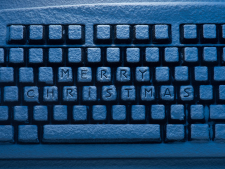 keyboard covered with snow with words Merry Christmas on keys illuminated with blue lightの写真素材