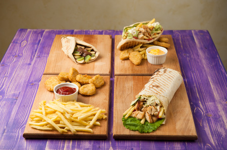nuggets and french fries, Turkish shawarma, Greek gyros and pita with chocolate and kiwi on a table for four personの写真素材