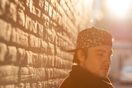 Handsome young man in a baseball cap lit by a warm backlight on a brick wall backgroundの写真素材