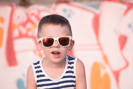 funny small kid wearing sunglasses and shirt on graffiti backgroundの写真素材