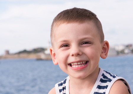 cheerful smiling little boy in sailor stripes singlet on sea and shore backgroundの写真素材