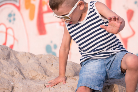 cute little boy in a sailor vest and shorts scrambles on a stone with graffiti wall backgroundの写真素材