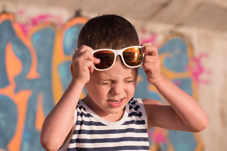 Little boy with white sunglasses with ocean sunset reflections squinted from the bright sunの写真素材