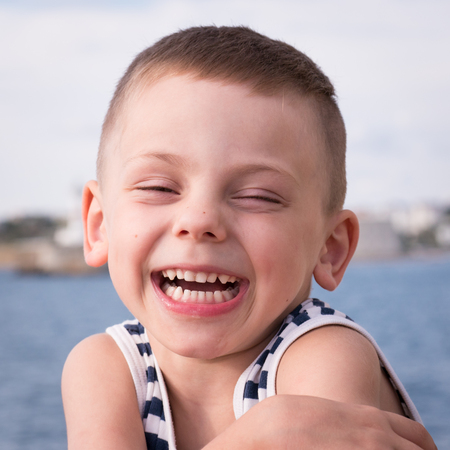 laughing little boy in sailor stripes singlet on sea and shore background in summerの写真素材