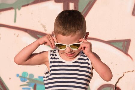 cute small boy with sunglasses and sailor stripes shirt on graffiti background looking downの写真素材