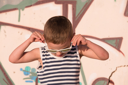 cheerful small boy with sunglasses and sailor stripes shirt on graffiti background looking downの写真素材