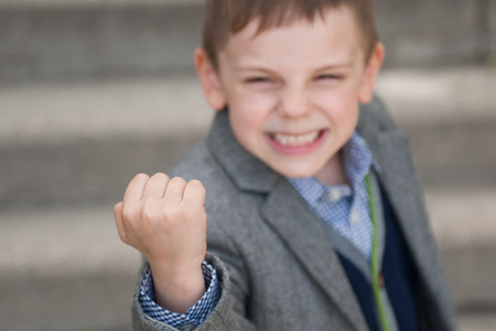Little boy with a grimace on his face threatens with his fist