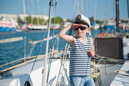 cute little boy captain wearing captain cap and sunglasses aboard luxury boatの写真素材