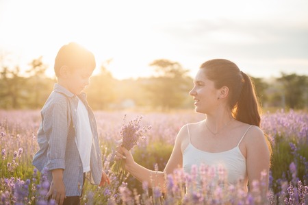Happy mother with bouquet of flowers looks at her child among the lavender fieldの写真素材