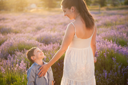 Happy smiling mother and child looking at each other with love standing among blooming lavender flower field at warm sunsetの写真素材