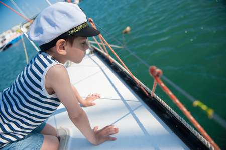 curious handsome little boy in a captains hat peeking over the side of the boatの写真素材