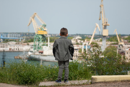 little kid in a jacket stands against the background of a sea portの写真素材