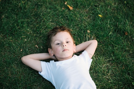portrait of cute little boy lying on green grassの写真素材