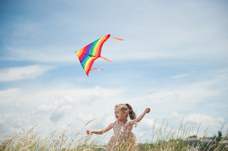 cheerful little girl with long hair holding flying kite in the field on summer sunny dayの写真素材