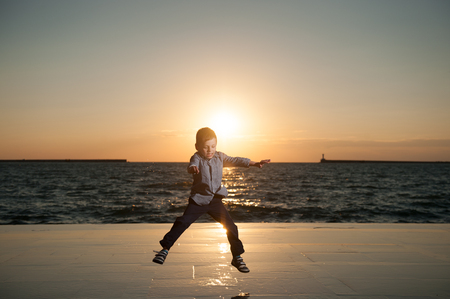 adorable little boy jumping on the background of the setting sun and the seaの写真素材