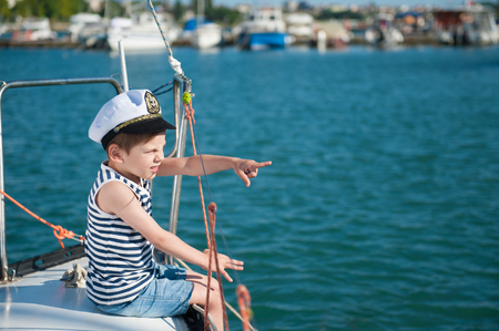 handsome little captain boy pointing with his finger to the distance sitting on luxury yacht in summer round-the-world tourの写真素材