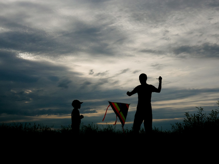 silhouettes of father and his small son flying the kite on the wonderful sunset background