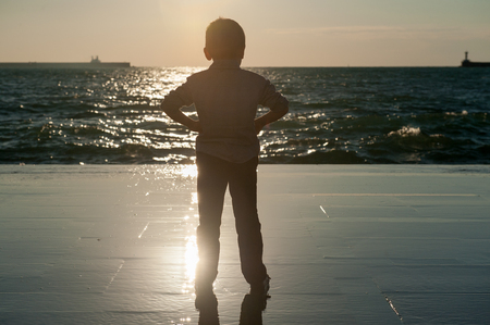 little kid looking at the storm sea at beautiful sunsetの写真素材