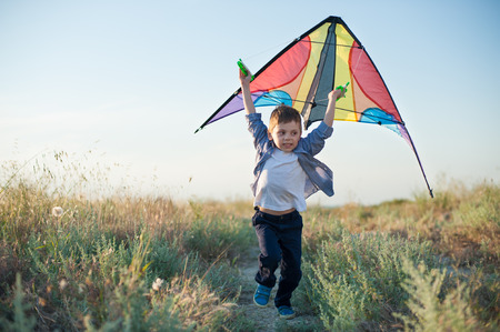 Beautiful boy in shirt running with a kite in hands on the path among field of plantsの写真素材