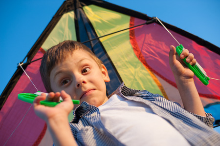 Surprised boy holding colorful kite on his shouldersの写真素材