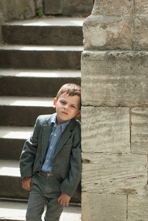 Beautiful little boy in a costume leaning on an ancient stone wallの写真素材