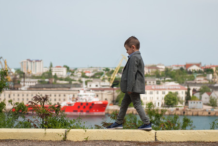 happy little boy in jacket walking on the curb in the background of the sea portの写真素材