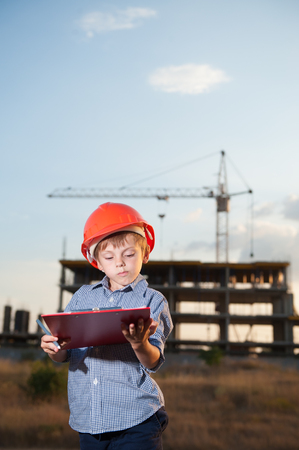 handsome little kid wearing orange helmet on building with crane background at sunsetの写真素材