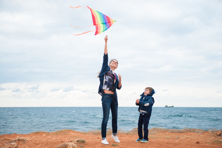happy mother and little child wearing autumn clothes playing kite on storm sea background in fallの写真素材