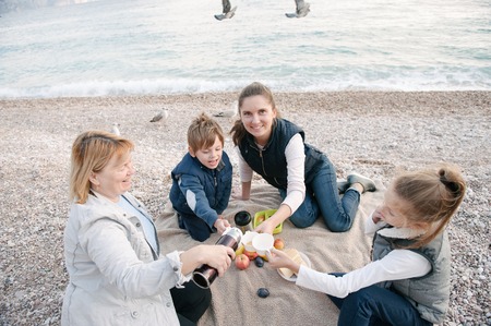 happy family consisting of grandma, mother and two children on picnic by the sea coast in overcast weatherの写真素材
