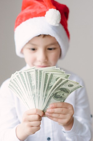happy cute boy in Santa hat holding hundred-dollar bills packの写真素材
