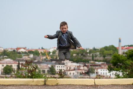 Little boy wearing suit jumping up on the cityscape backgroundの写真素材