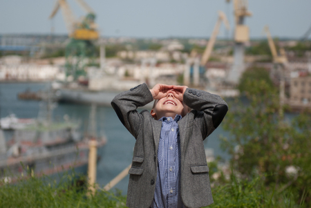 Smiling little boy looking up holding hands in the form of binoculars on the background of sea portの写真素材
