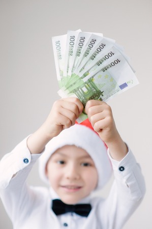 boy in Santa hat holds a certain amount of Euro banknotes above his headの写真素材