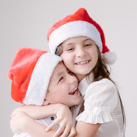 two smiling kids in Santa hats huggingの写真素材