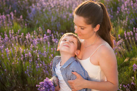 happy beautiful mother and smiling child on the blooming lavender flower field lit by warm sunset lightの写真素材