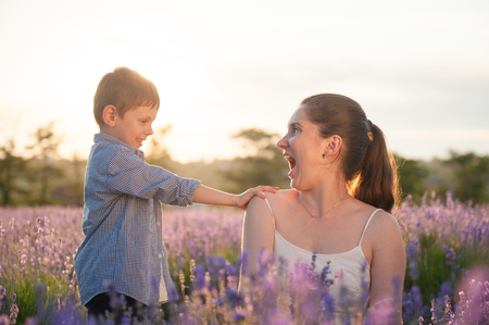 Emotional beautiful mother and her son touching her shoulder with tenderness on the purple lavender field at warm summer sunsetの写真素材
