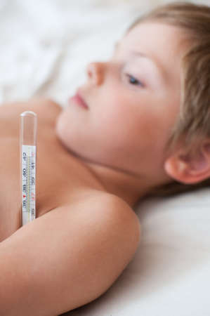 lying sick little caucasian boy with thermometer in the armpit