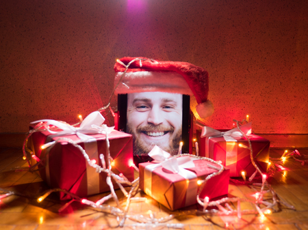 tablet with cute bearded male on screen and santa cap on it with Christmas attributes aroundの写真素材