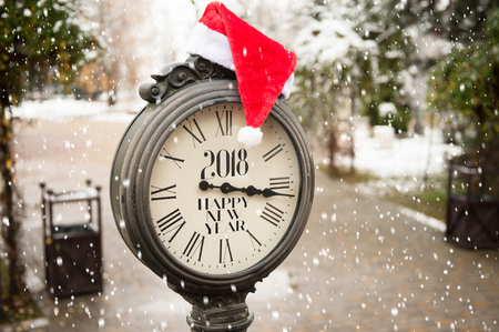 vintage street clock with title Happy New Year 2018 and Santa Claus hat on them with falling snowflakesの写真素材