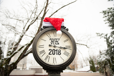 vintage street clock with the inscription Happy New Year 2018 and Santa Claus hat on them outdoorsの写真素材