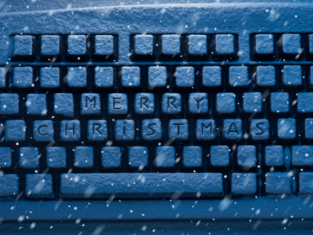 computer keyboard with text merry christmas on buttons covered with snow illuminated by blue neon...