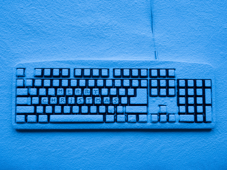 computer keypad covered with snow illuminated by blue neon light with text merry christmasの写真素材