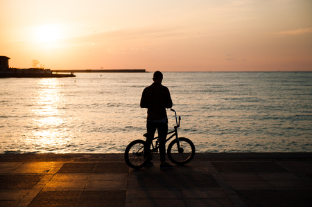 silhouette of a young man with a bike against the sea in the cityの写真素材