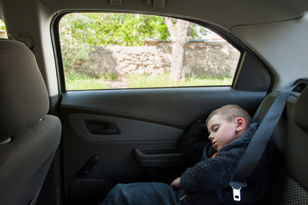 cute small boy sleeping on back seat of car near windowの写真素材