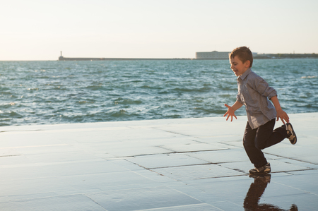 funny cute little boy running along the sea coast in the cityの写真素材