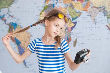 pretty little caucasian girl holding vintage camera and her pigtails on background of world mapの写真素材