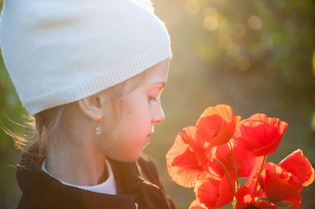dreamy little girl in white woolen hat with bouquet of orange poppy flowers backlit with spring sunsetの写真素材