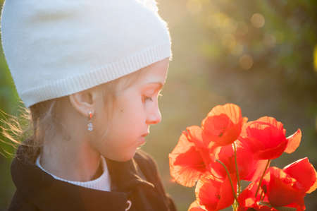 dreamy little girl in white woolen hat with bouquet of orange poppy flowers backlit with spring sunsetの写真素材