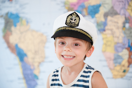 happy adorable caucasian smiling kid in captain hat on world map backgroundの写真素材